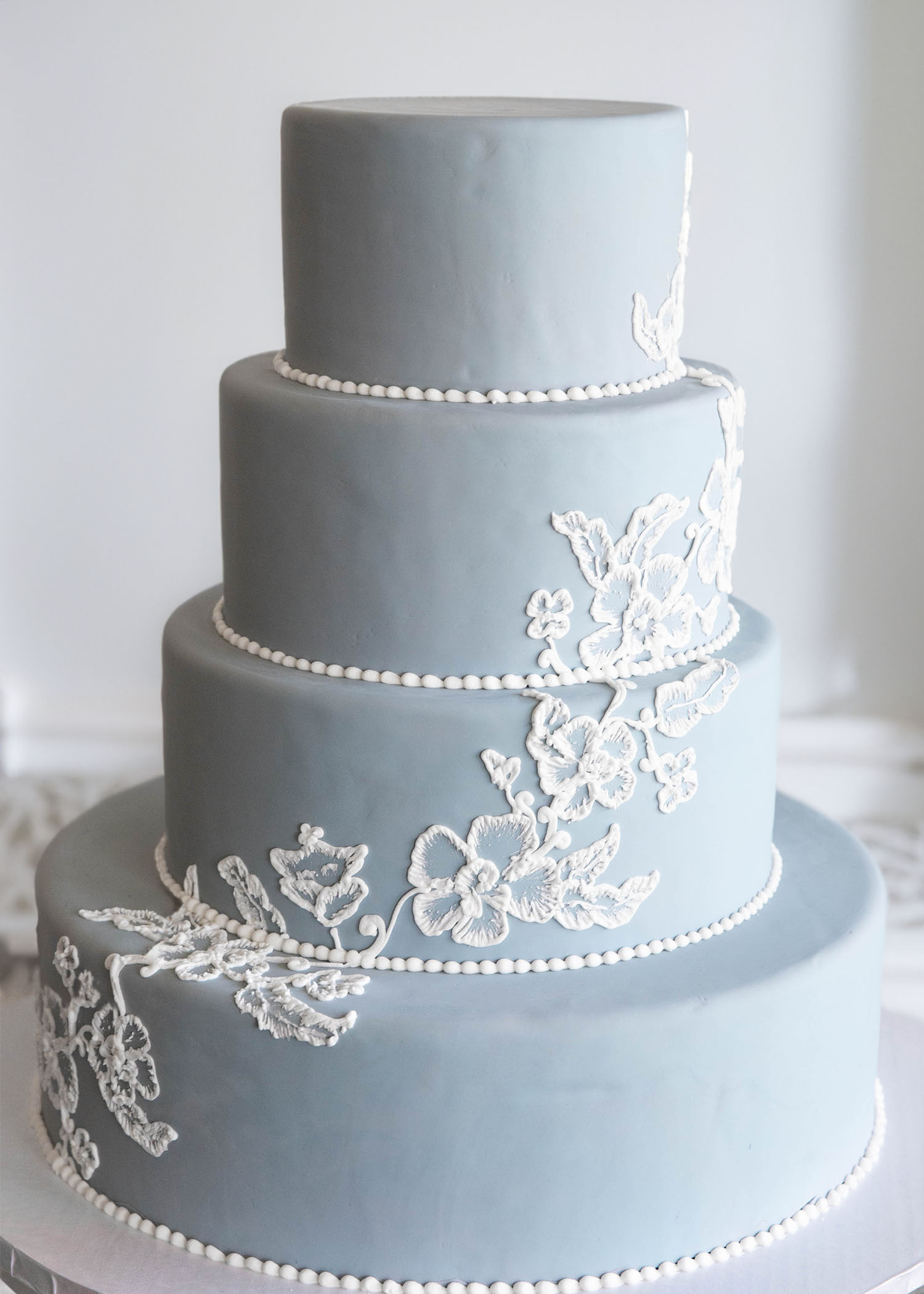 Painted floral design cascading down the cake. Small beaded border on all four tiers. Minimal, elegant, and modern wedding cake design by Bethel Bakery Pittsburgh PA.