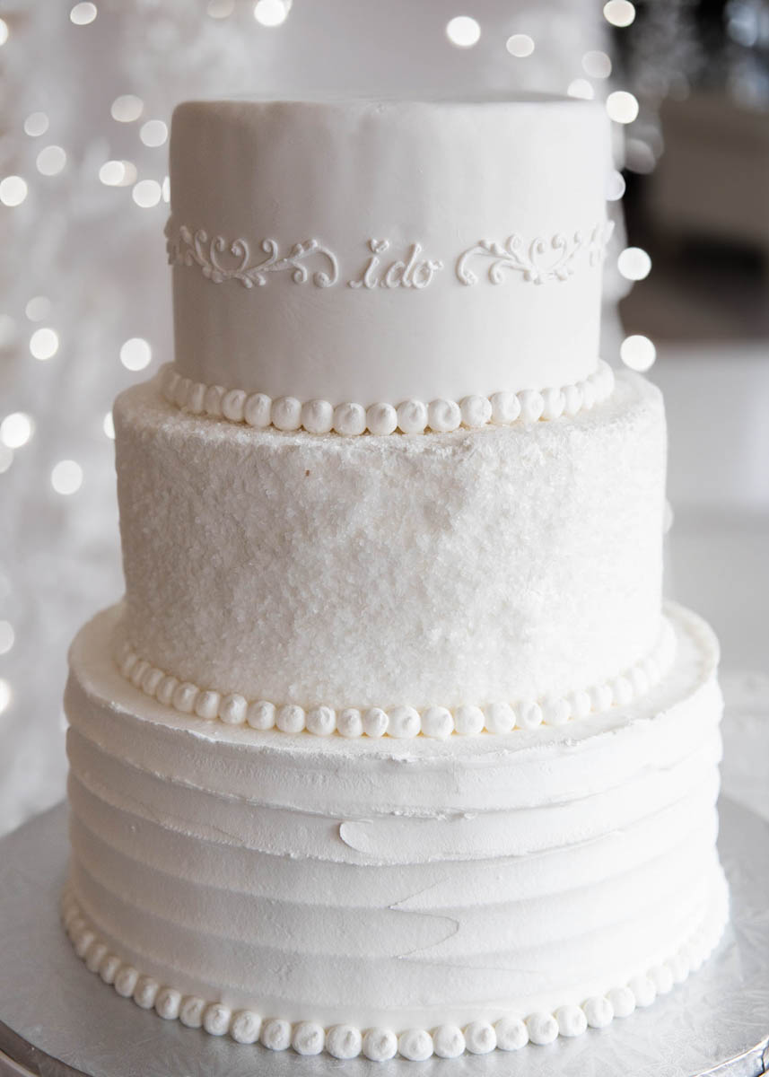 Small spatula combing on bottom tier, crystalized sugar and glitter middle tier, "I do" scroll work on top tier. beaded border on all tiers. All white French Buttercream.